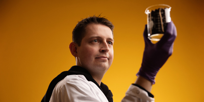 Professor Jarad Anderson wearing rubber gloves while examining material in a beaker