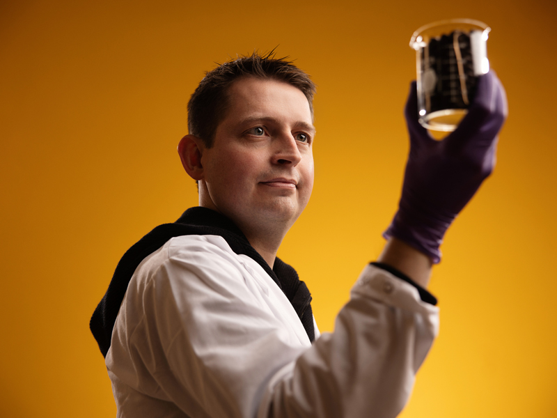 Professor Jarad Anderson wearing rubber gloves while examining material in a beaker