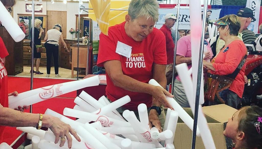 Middle-aged volunteer handing out Forever True-branded pool noodles to children