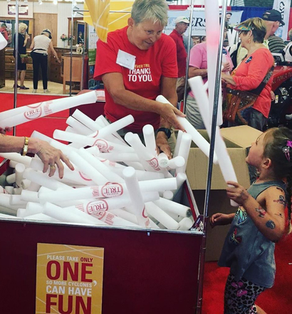 Middle-aged volunteer handing out Forever True-branded pool noodles to children