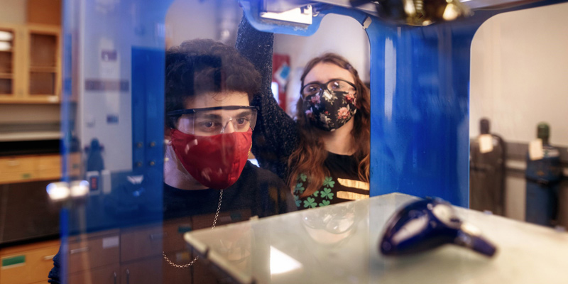 Two students watching an object take shape in a 3-D printer
