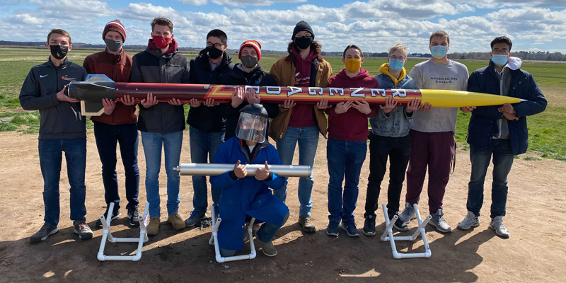 Members of Cyclone Rocketry pose with rocket in an open area outdoors