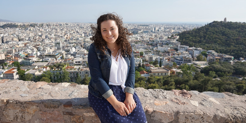 Sophie Catus sitting on a brick wall with view of a European city in the background