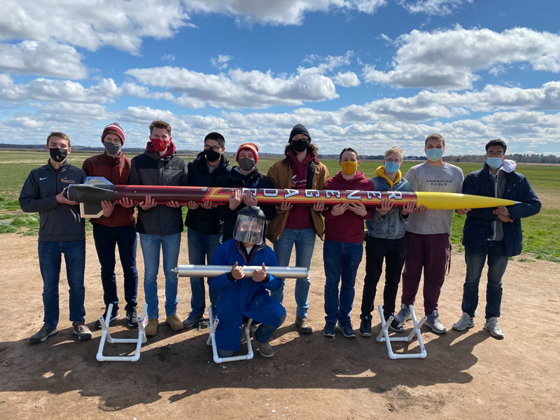 Members of Cyclone Rocketry pose with rocket in an open area outdoors