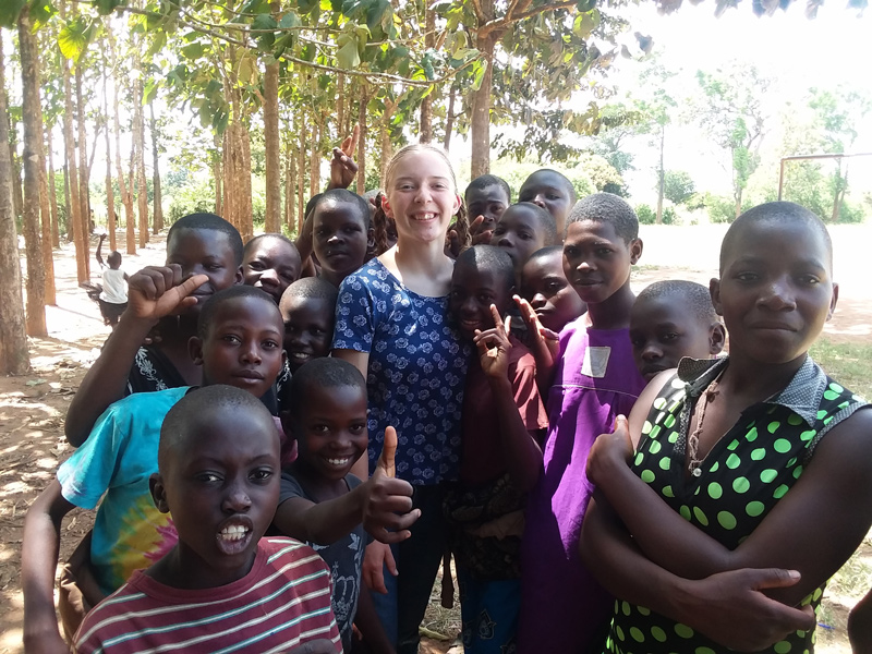 Grace Jakes poses with children and adolescents in rural Uganda